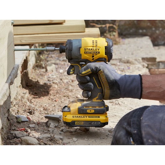 STANLEY SFMCF810D2K impact driver held by gloved hand, driving screw into wooden beam outdoors.