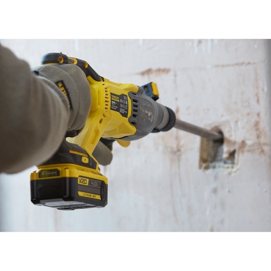 STANLEY SFMCH900M22 rotary hammer drill in use drilling into a concrete wall, close-up of tool and battery.