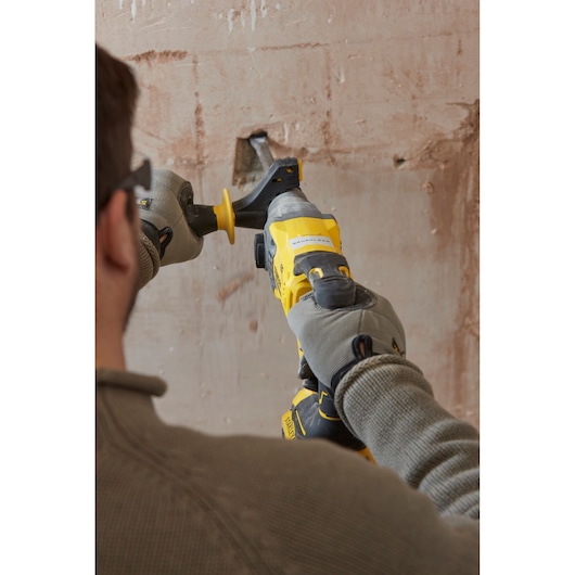 STANLEY SFMCH900M22 rotary hammer in use on wall, close-up showing gloved hands and tool angles.