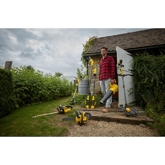 STANLEY SFMCHT855B garden tool collection with yellow-black hedge trimmer, chainsaw, blower, and grass trimmer outdoors.