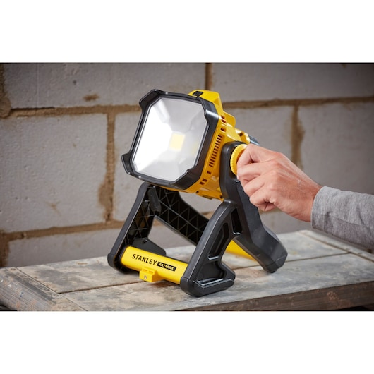 STANLEY SFMCL030B LED work light, yellow and black, adjustable stand, photo shows hand rotating knob.