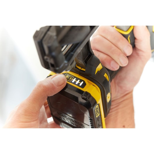 STANLEY SFMCN616D2K cordless nailer close-up, yellow and black, user hand pressing battery indicator.