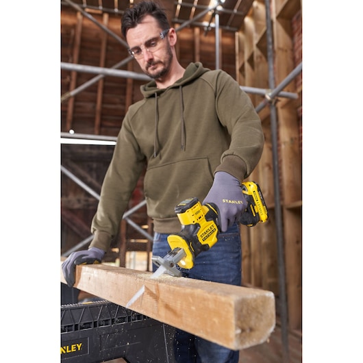 STANLEY SFMCS305B compact yellow cordless saw cutting a wooden beam, held by person wearing gloves.
