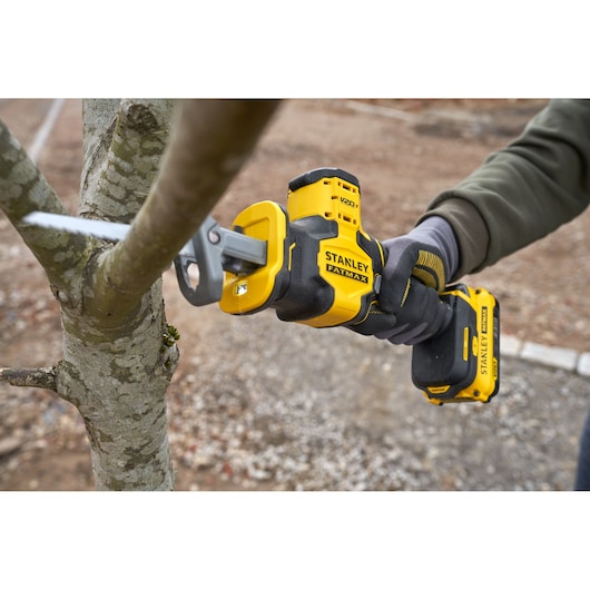 Stanley SFMCS305B cordless reciprocating saw cutting tree branch outdoors, close-up view.