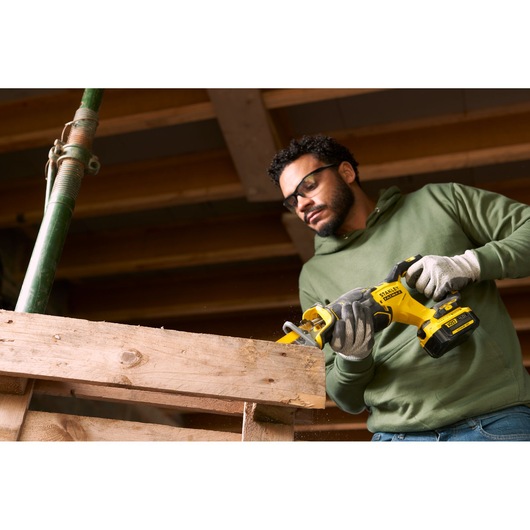 Photo of a person using a STANLEY SFMCS310B cordless reciprocating saw to cut a wooden beam on a construction site.