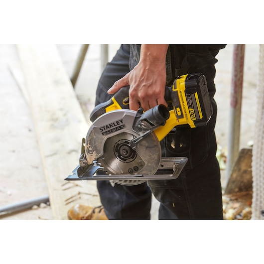STANLEY SFMCS500B cordless circular saw held by person, yellow and black design, construction context.