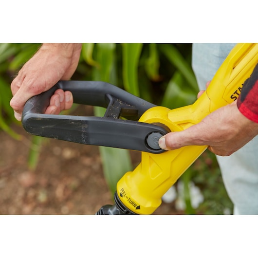 Close-up of STANLEY SFMCST933B string trimmer handle being adjusted, yellow and black details, outdoor setting.