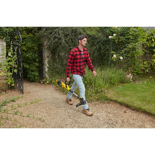 STANLEY SFMCST933B string trimmer held by a person outdoors on a garden path.