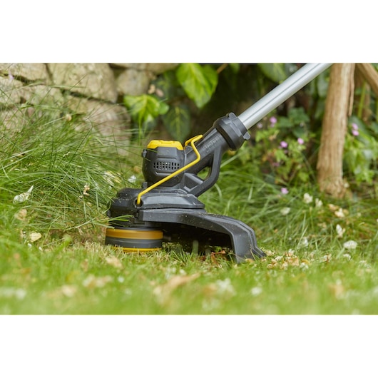 STANLEY SFMCST933M1 grass trimmer cutting grass in garden, close-up side view.