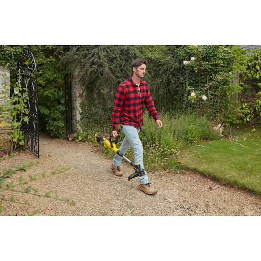 Photo of person holding STANLEY SFMCST933M1 cordless string trimmer, walking on gravel garden path.