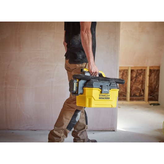 Person carrying STANLEY SFMCV002B portable yellow vacuum with black hose in a construction site.