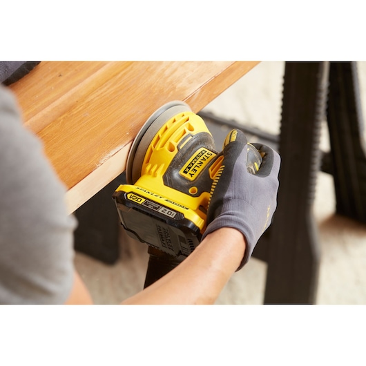 Photo of STANLEY SFMCW220D1S cordless sander being used on wooden surface.