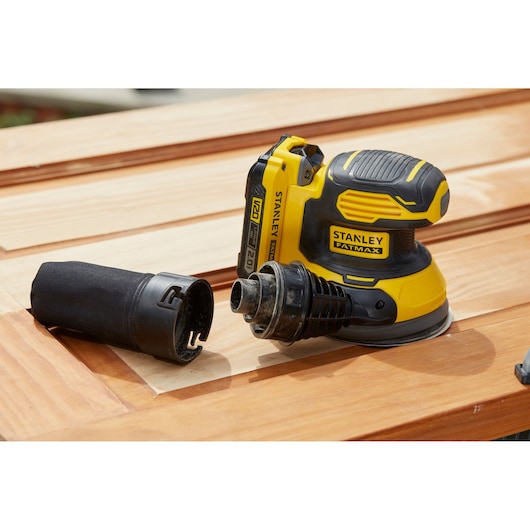 STANLEY SFMCW220D1S cordless sander on wood surface with dust collector detached, shown from side angle.