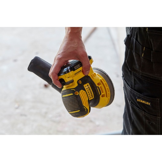Photo of STANLEY SFMCW220D1S cordless random orbital sander in hand, yellow and black color.