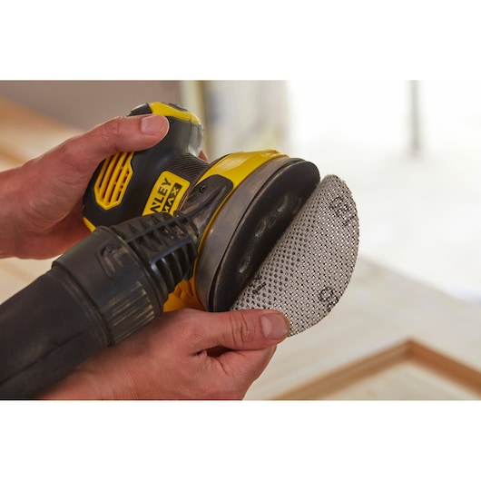 Photo of hands attaching a sanding disc to a STANLEY SFMCW220D1S cordless sander, product in use.