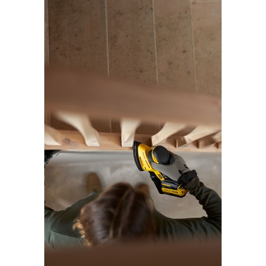 Photo of STANLEY SFMCW221B sander in use on a wooden staircase, hand holding tool for sanding railing.