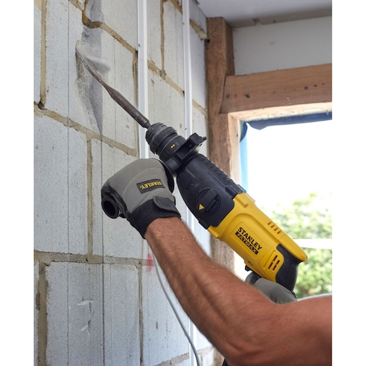 Photo of STANLEY SFMEH210K rotary hammer in use chiseling a concrete block wall, close-up action view.