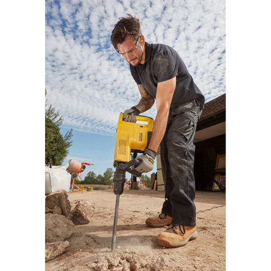 Photo of a person using STANLEY SFMEH230K-QS demolition hammer on outdoor concrete, construction scene visible.