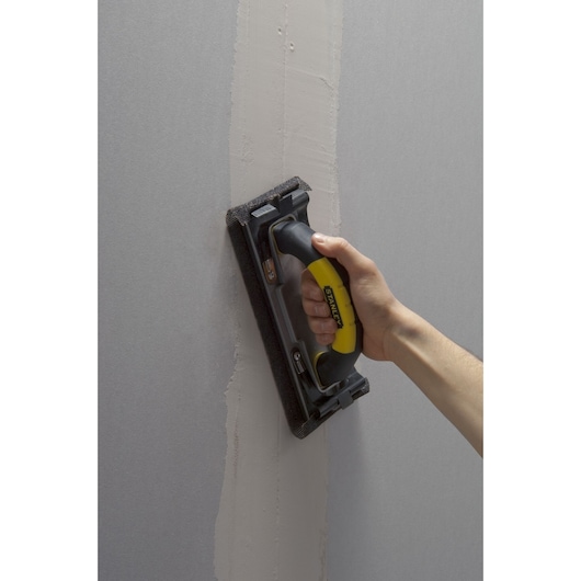 Photo of STANLEY STHT0-05927 hand sander with black and yellow handle sanding wall surface.