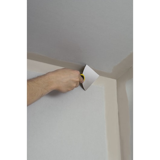 STANLEY STHT0-26089 putty knife in use spreading compound in a wall corner.