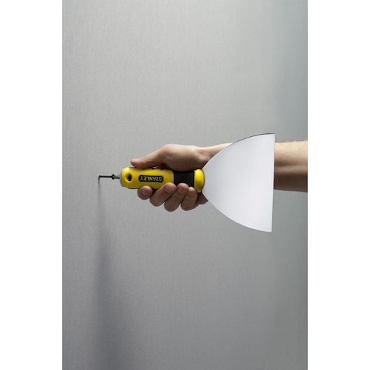 STANLEY STHT0-28034 putty knife with yellow and black handle, side view held by hand against a wall.