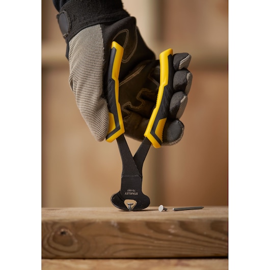 Photo of STANLEY STHT0-75067 yellow-handled end cutting pliers held by gloved hand, removing nail from wood.