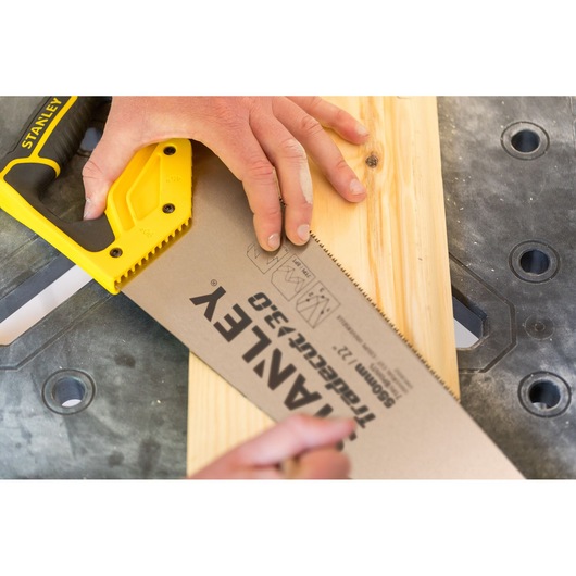 STANLEY STHT1-20353 handsaw with yellow handle cutting wooden plank on workbench.