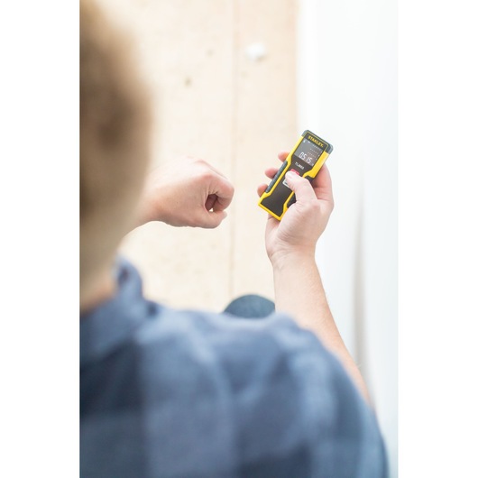 STANLEY STHT1-77032 laser distance measurer held by person, black and yellow design, product in use.