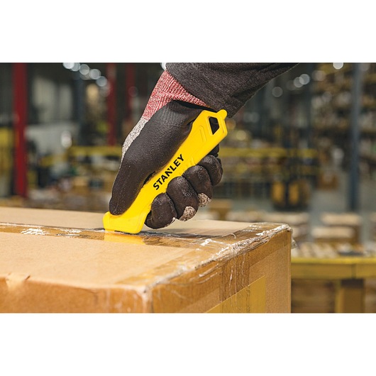STANLEY STHT10355-1 safety utility knife cutting tape on a cardboard box in a warehouse, close-up.