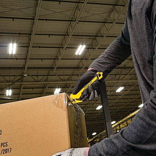 Stanley STHT10356 utility knife cutting box tape in warehouse, close view, person wearing gloves.