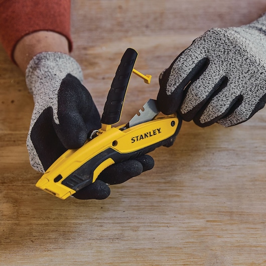Photo of STANLEY STHT10479-0 yellow utility knife with black handle held by gloved hands on wooden surface.