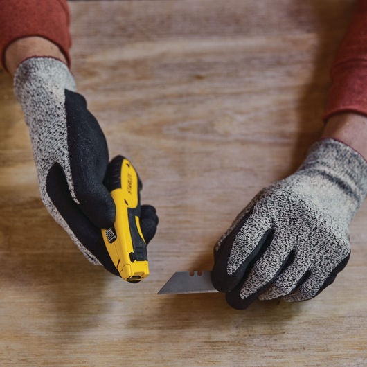 STANLEY STHT10479-0 utility knife and blade held by gloved hands on wooden surface.