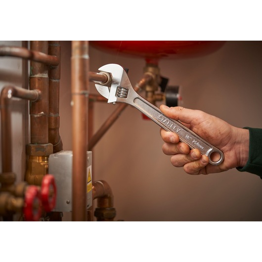 STANLEY STHT13122-0 adjustable wrench used on copper pipes in plumbing setting.