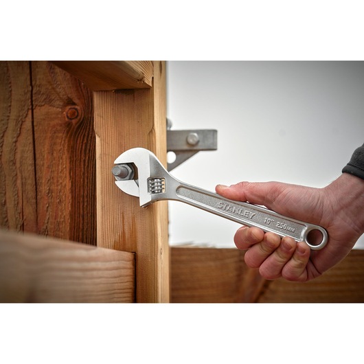 Stanley STHT13122-0 adjustable wrench used on bolt in wooden structure, close-up photography.