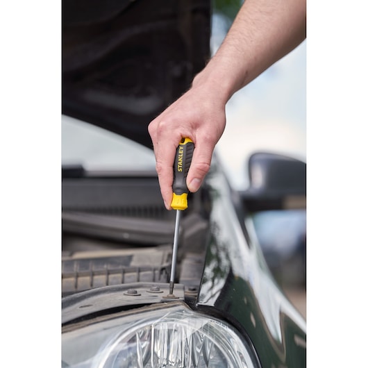 STANLEY STHT16179-0 screwdriver used on a car engine, black and yellow ergonomic handle.