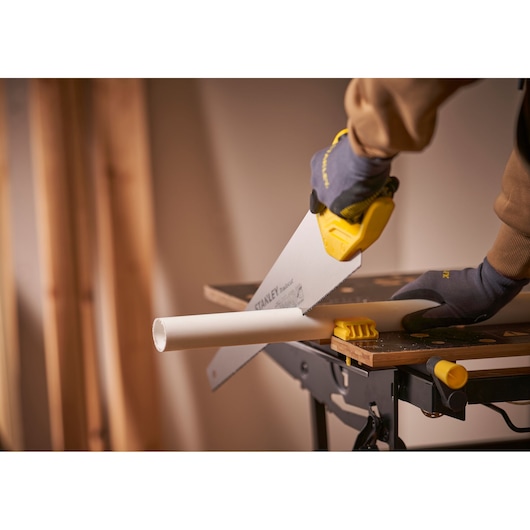 STANLEY STHT20351-1 hand saw cutting white pipe on workbench, close-up photography.