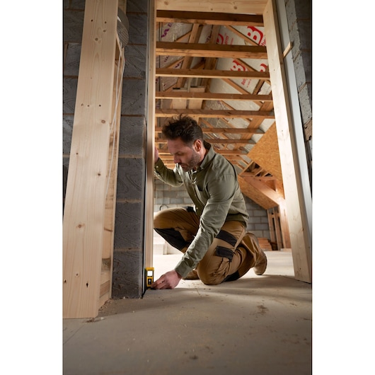 STANLEY STHT77065-0 laser distance measurer in use in a construction site, user measuring from floor to wall.