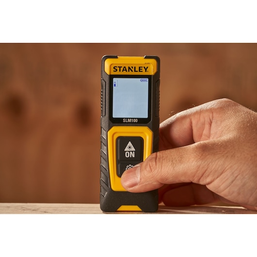 STANLEY STHT77100-0 laser distance measurer handheld, shown activated in a person’s hand, close-up view.