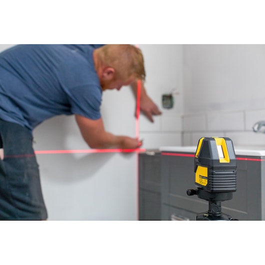 STANLEY STHT77514-1 laser level device projecting red lines for precise wall alignment in a bathroom renovation.