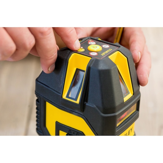 Photo of STANLEY STHT77514-1 laser level with buttons, close-up, person pressing power button.