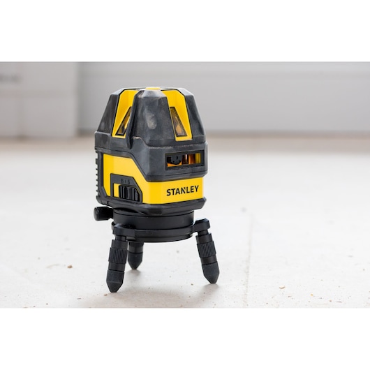 Photo of STANLEY STHT77514-1 laser level tool with tripod legs, yellow and black, on floor.