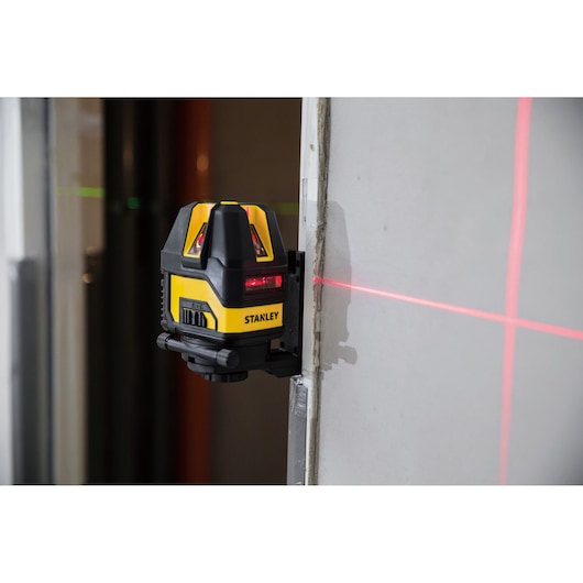 STANLEY STHT77514-1 laser level projecting red lines onto a wall, mounted during indoor construction work.