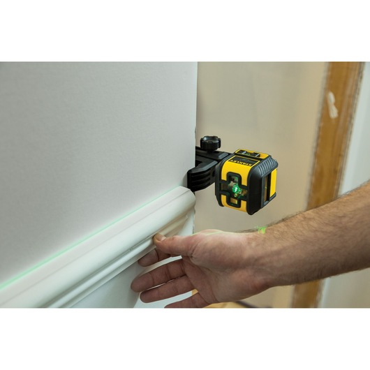 STANLEY STHT77592-1 laser level tool projecting green line on wall during baseboard installation.