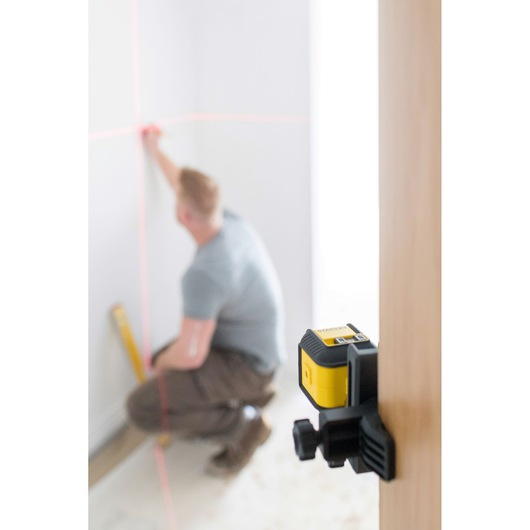 Photo of STANLEY STHT77648-1 laser level on clamp projecting red horizontal and vertical lines in a room.