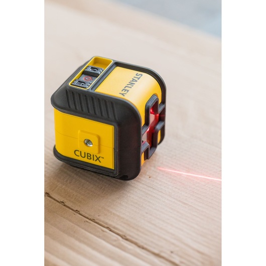 STANLEY STHT77648-1 CUBIX laser level, compact yellow and black tool, projecting red laser line on wood surface.