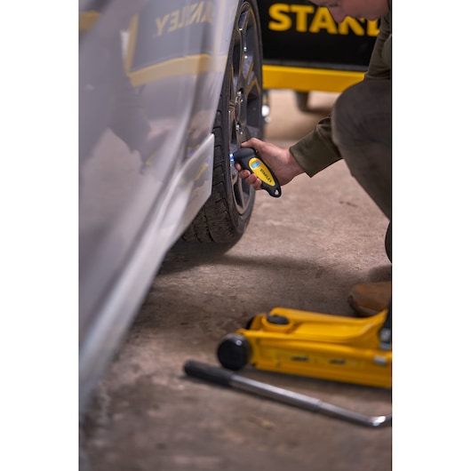 STANLEY STHT80874-0 tire pressure gauge used on car wheel, yellow and black tool, automotive setting.