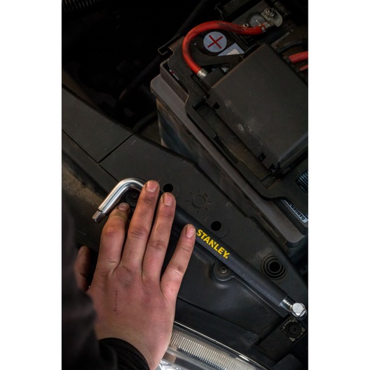 Photo of STANLEY STHT80879-0 hex key in use on a car battery, close-up view with hand holding tool.