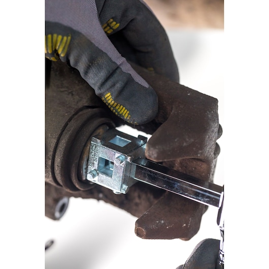 Photo of STANLEY STHT80883-0 brake caliper tool in use, close-up on automotive part with gloved hand.