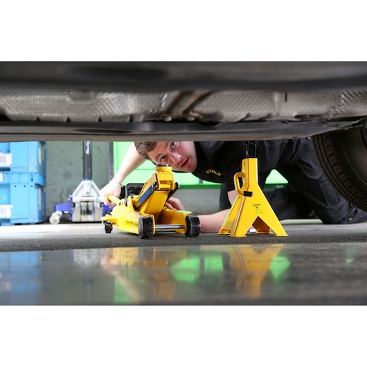 STANLEY STMT81255-1 yellow car jack and jack stand under a vehicle, side angle photo.