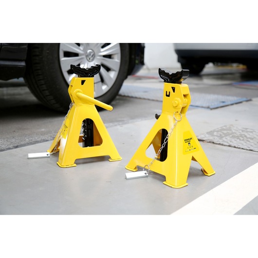 STANLEY STMT81255-1 yellow automotive jack stands on garage floor, side angle, near parked vehicles.